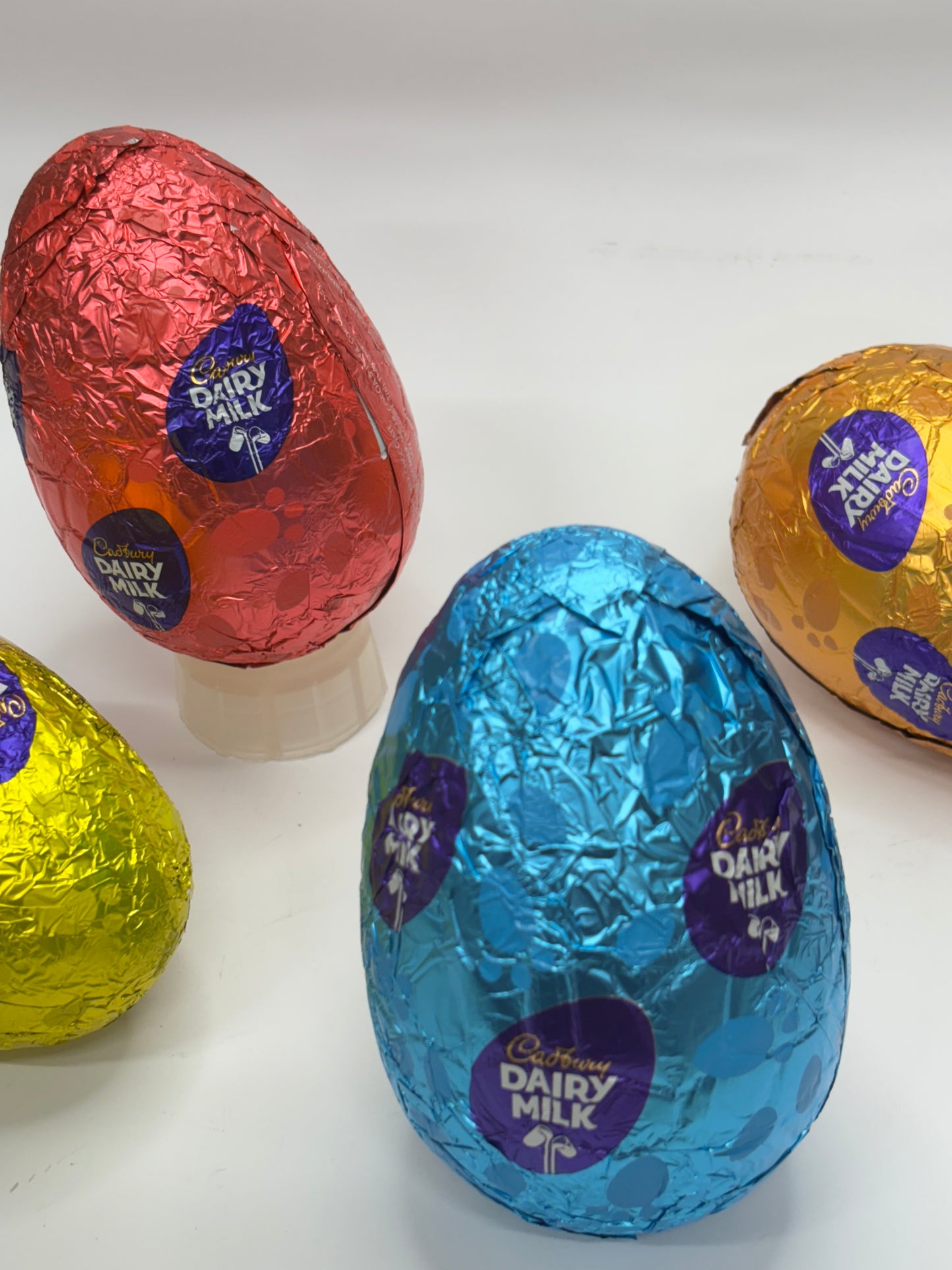 Colorful foil-wrapped milk chocolate egg in blue, surrounded by other chocolate eggs in red, yellow, and gold