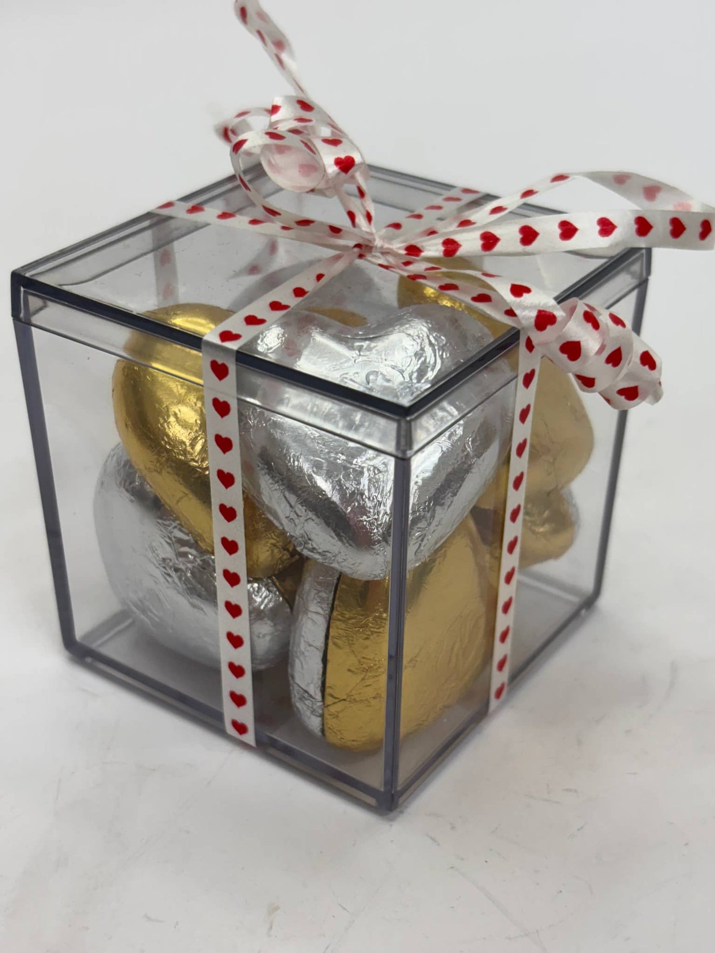 Clear gift box filled with pink lady chocolate hearts wrapped in silver and gold foil