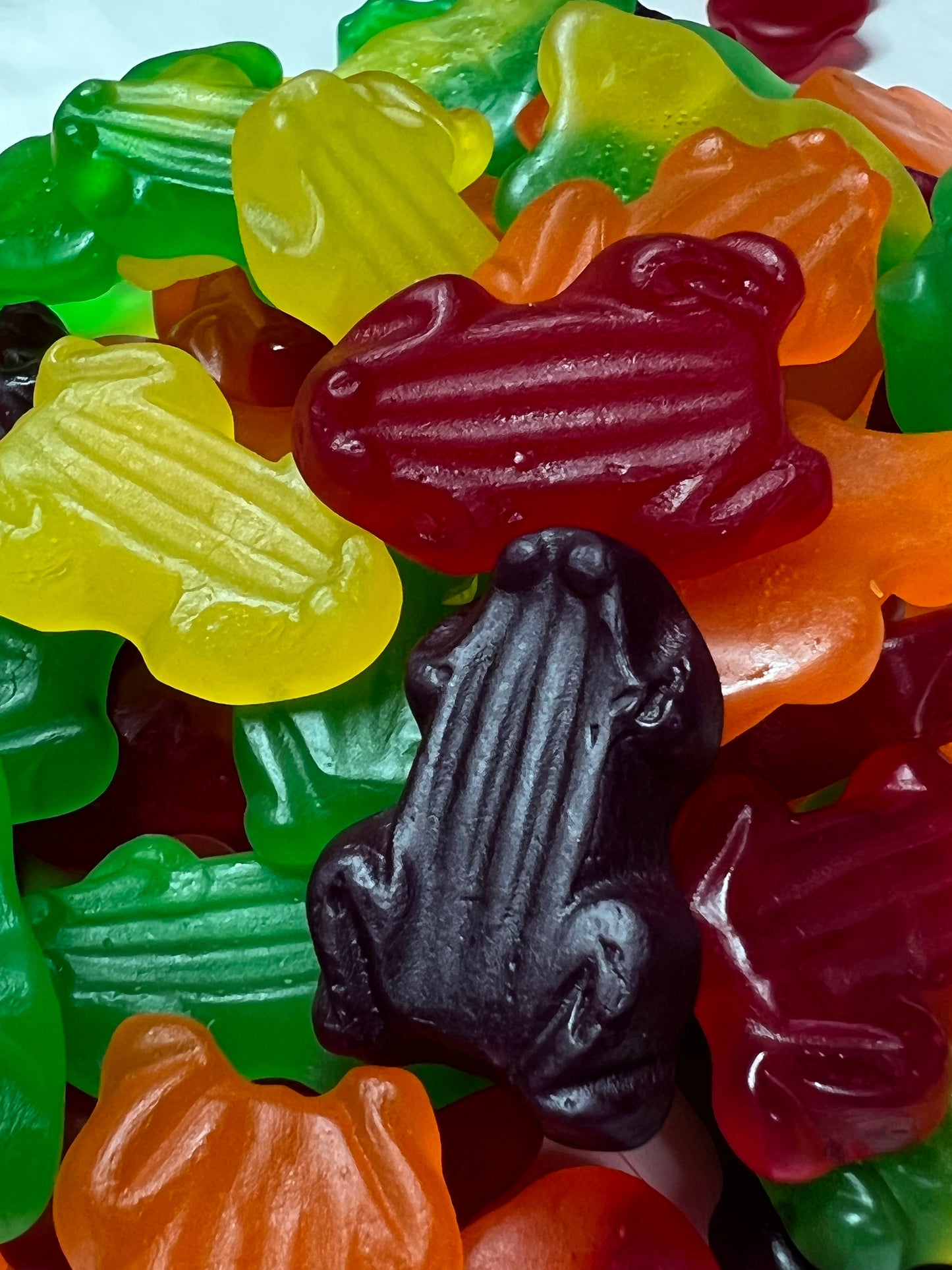 Colorful gummy frog candy in red, yellow, green, orange, and black shapes tightly packed together
