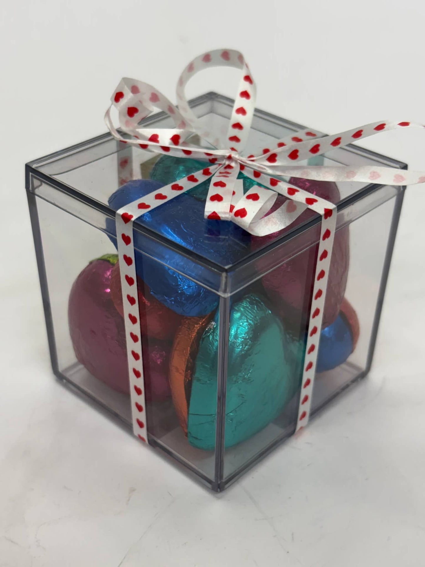 Clear gift box filled with colorful pink lady chocolate hearts wrapped in a patterned ribbon